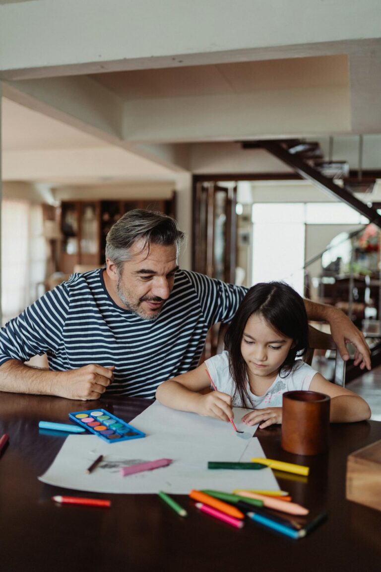 Father and daughter enjoying creative time drawing and painting together at a table.