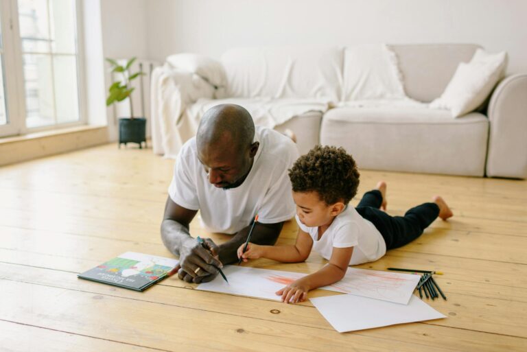 Father and son spend quality time drawing together on a wooden floor at home.